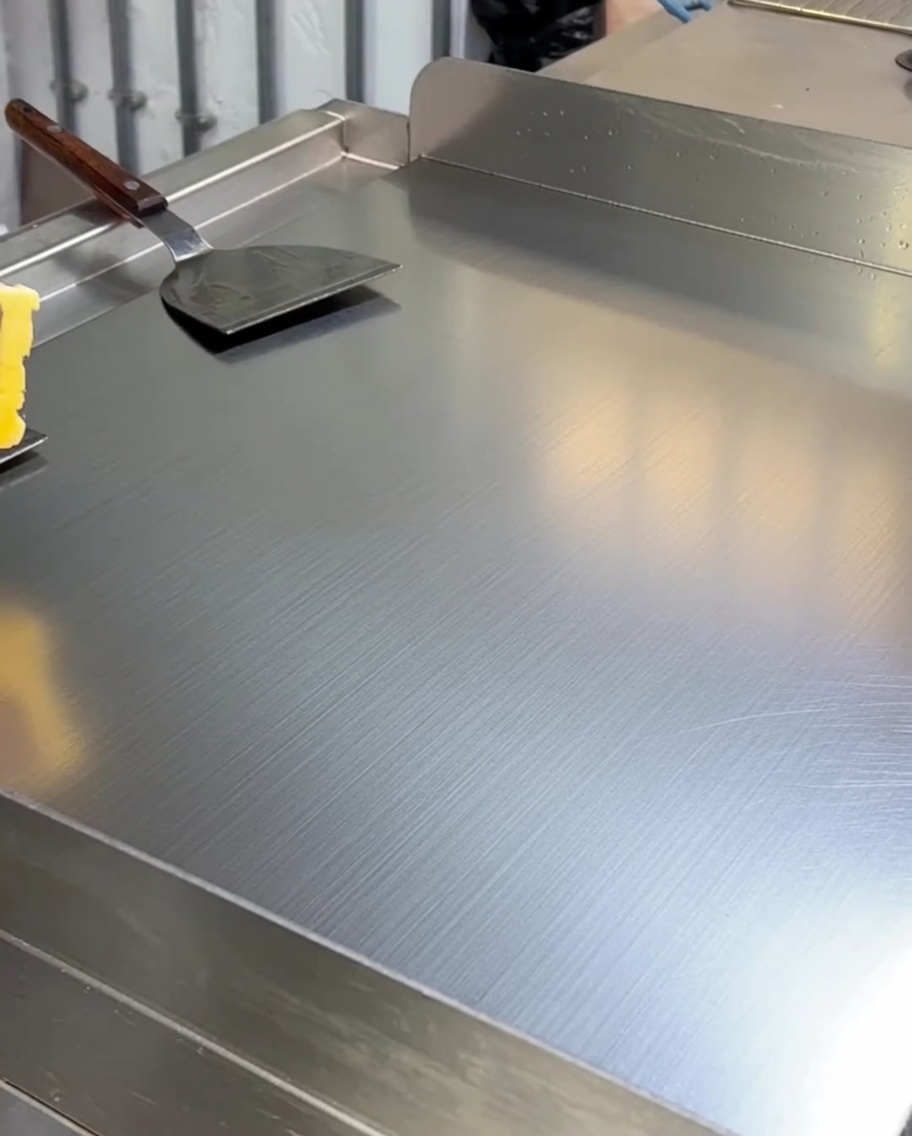 Beurre jaune fondant et enrobant la surface dune plaque de cuisson chaude en inox.