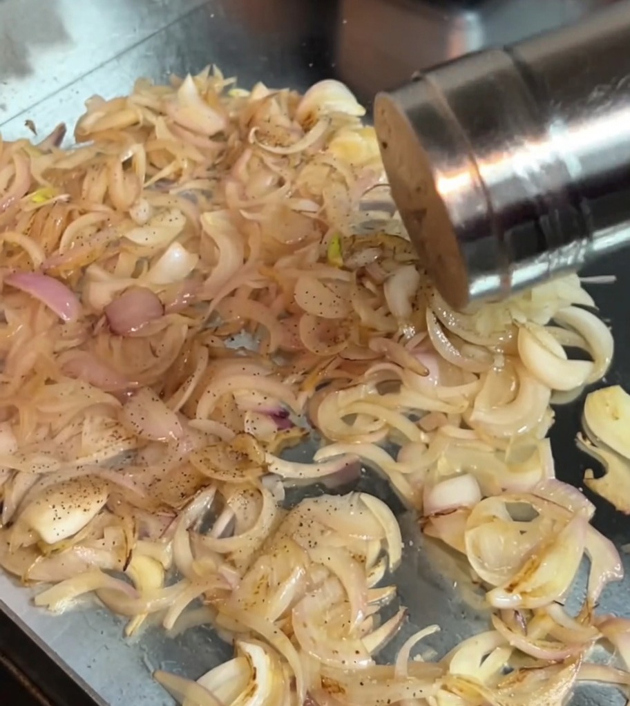 Sel et poivre noir saupoudrés sur les oignons en train de sauter dans la poêle.