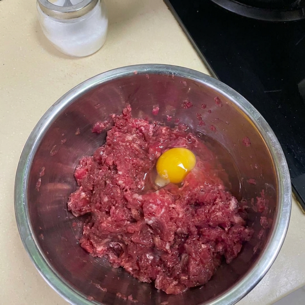 Bœuf haché mélangé avec des épices et un œuf dans un bol en métal.