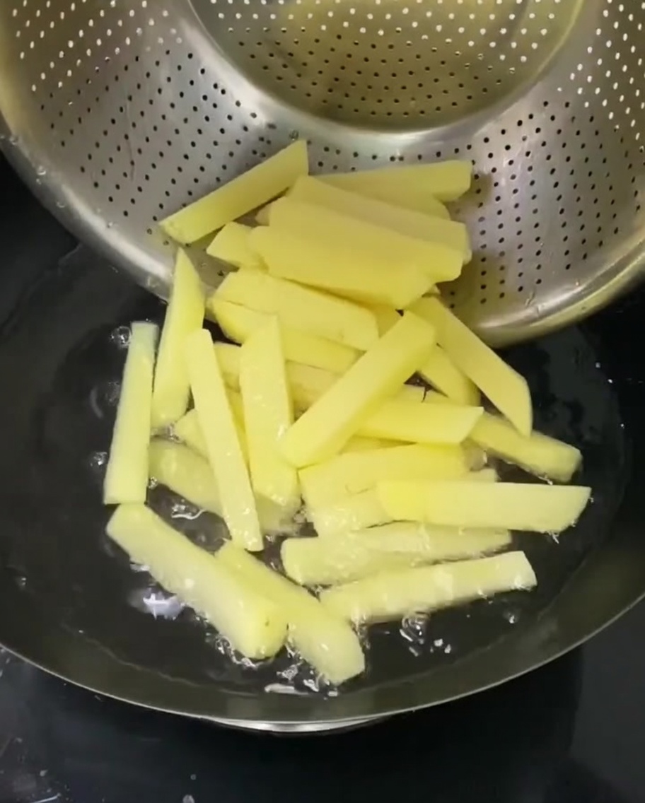 Frites de pommes de terre bouillant dans une passoire en métal immergée dans une casserole deau chaude.