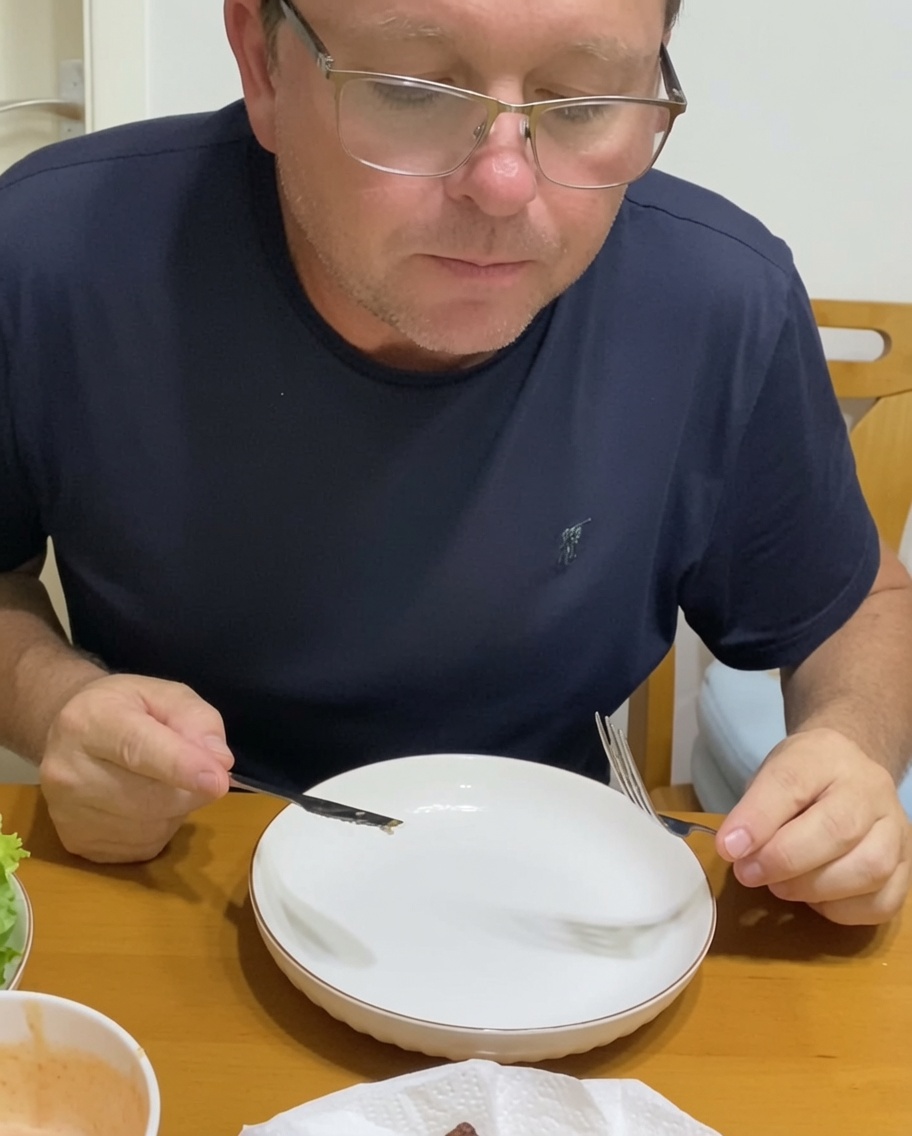Une personne assemblant un burger sur une assiette, ajoutant des oignons caramélisés et des légumes frais sur un steak de bœuf dans un pain.