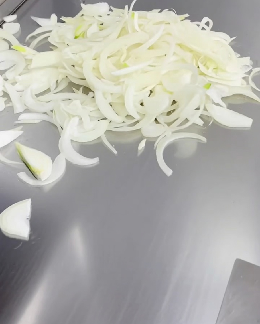 Oignons émincés étalés sur une plancha chaude.
