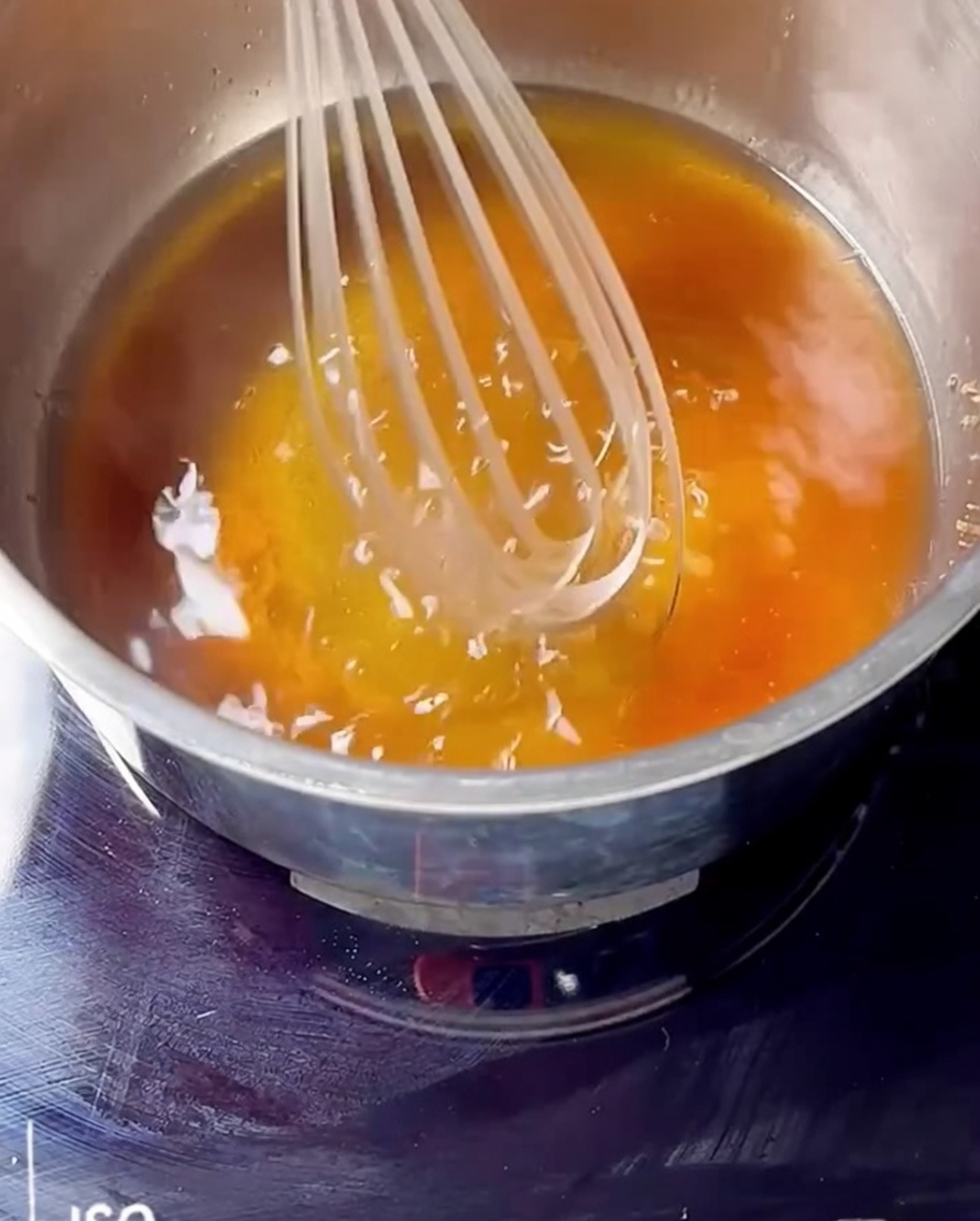 Fouet mélangeant confiture de cerise, bourbon et sucre dans une casserole.