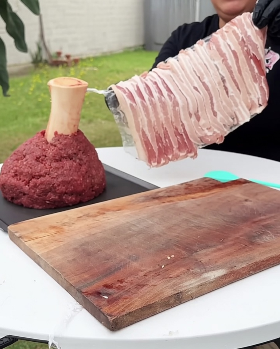 Un bloc de bœuf haché carré enveloppé soigneusement de tranches de bacon cru.