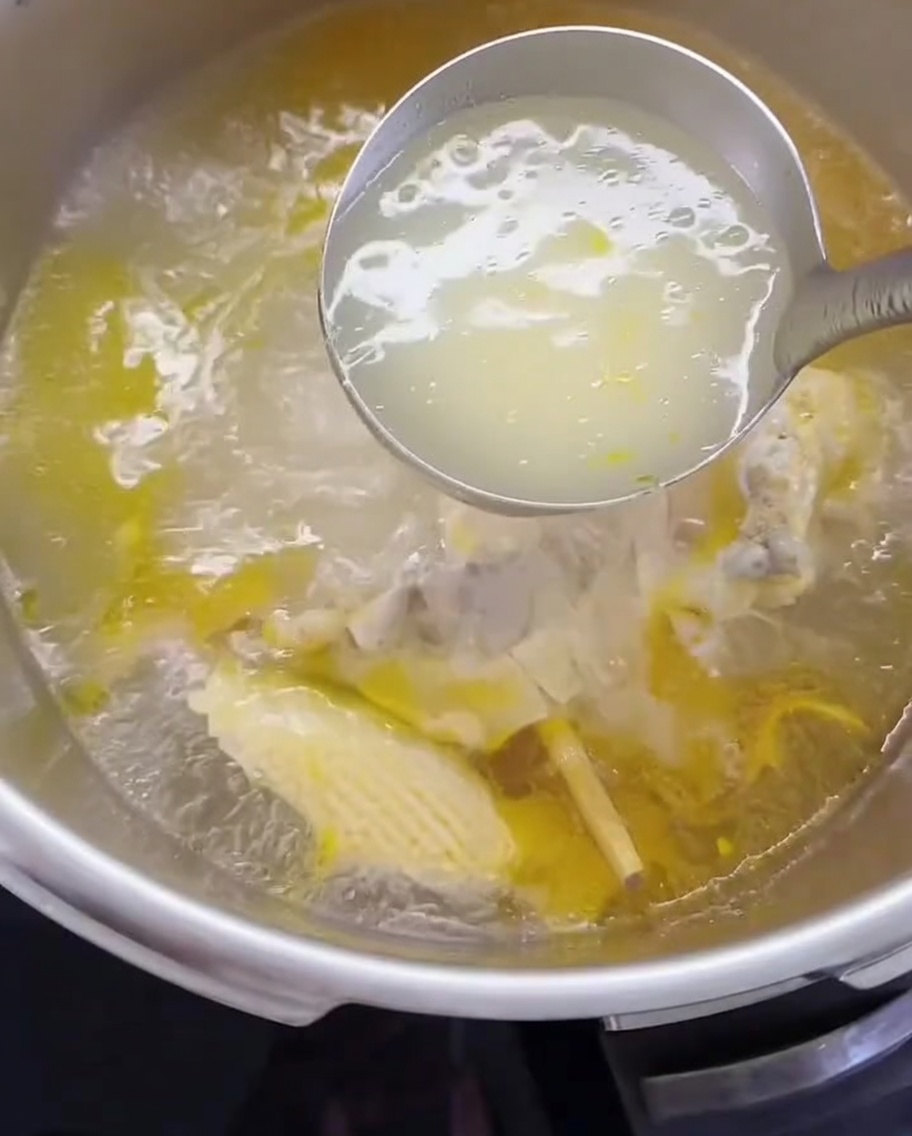 Une louche transférant le bouillon de poulet et la viande effilochée dans une casserole.