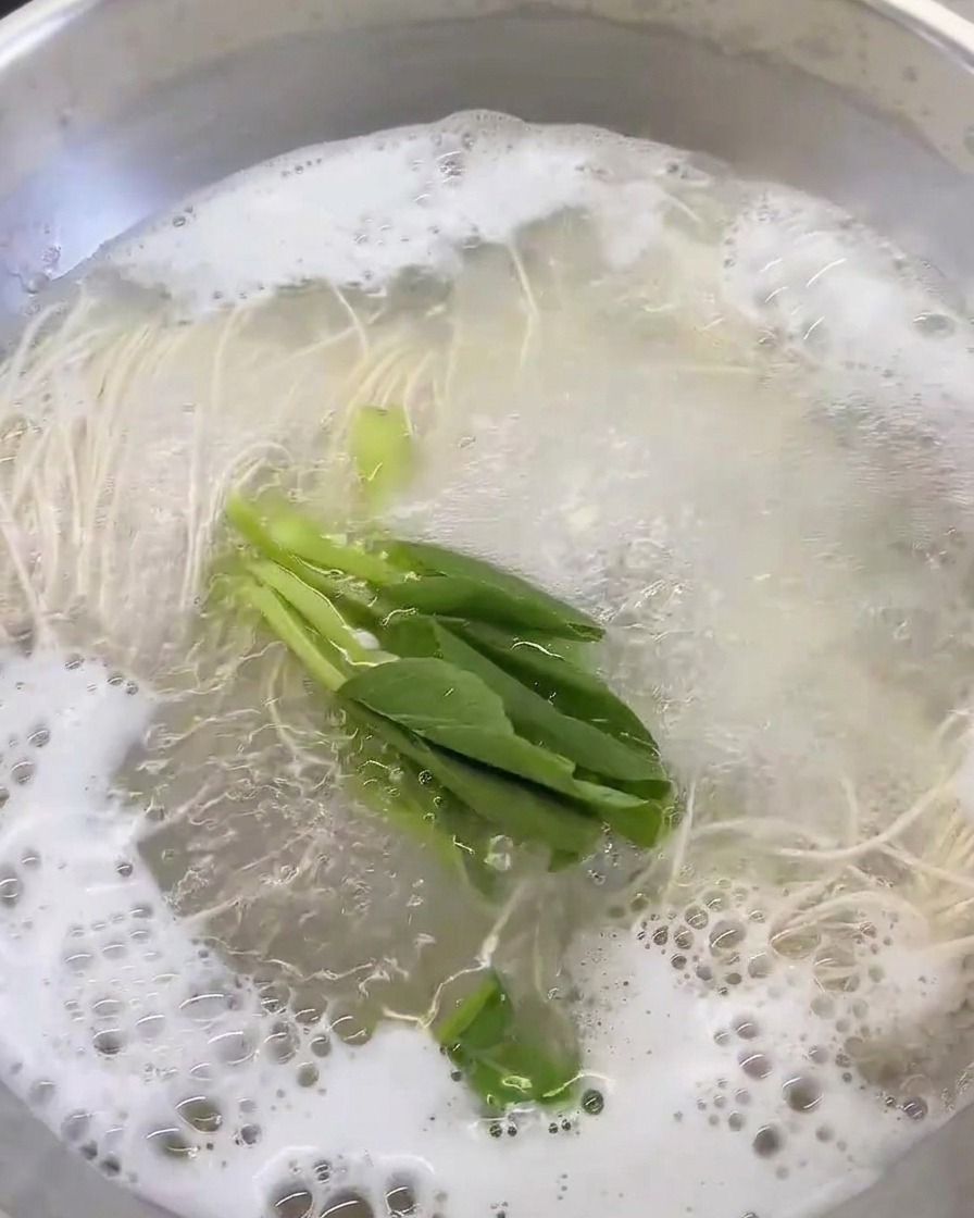 Légumes verts frais ajoutés dans la casserole de bouillon et nouilles bouillantes.