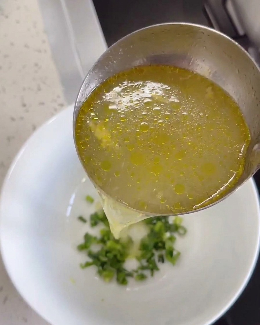 Bouillon de poulet chaud versé dans un bol contenant du gingembre et de la coriandre.
