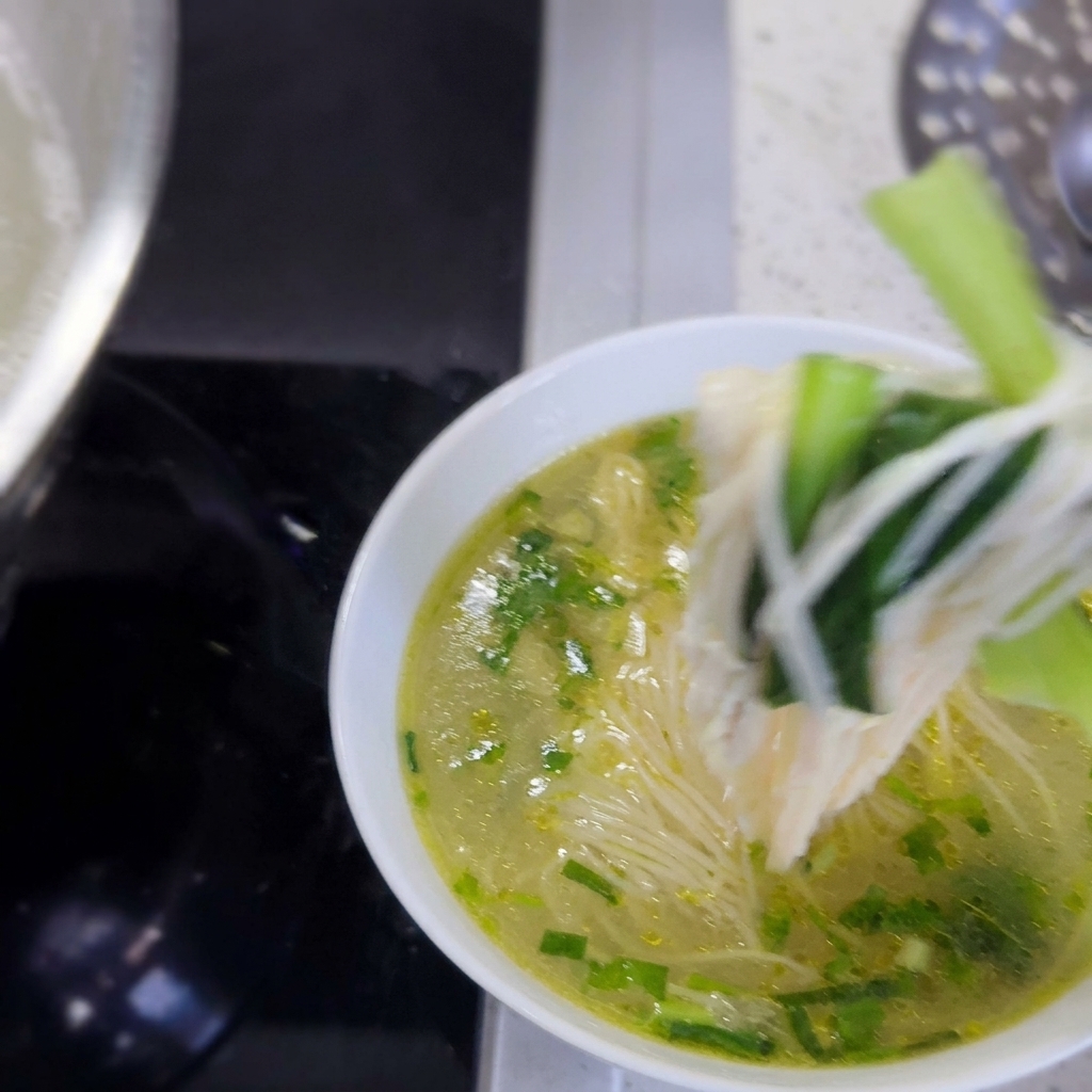 Un bol rempli de nouilles chaudes, de légumes verts et de poulet effiloché prêt à servir.