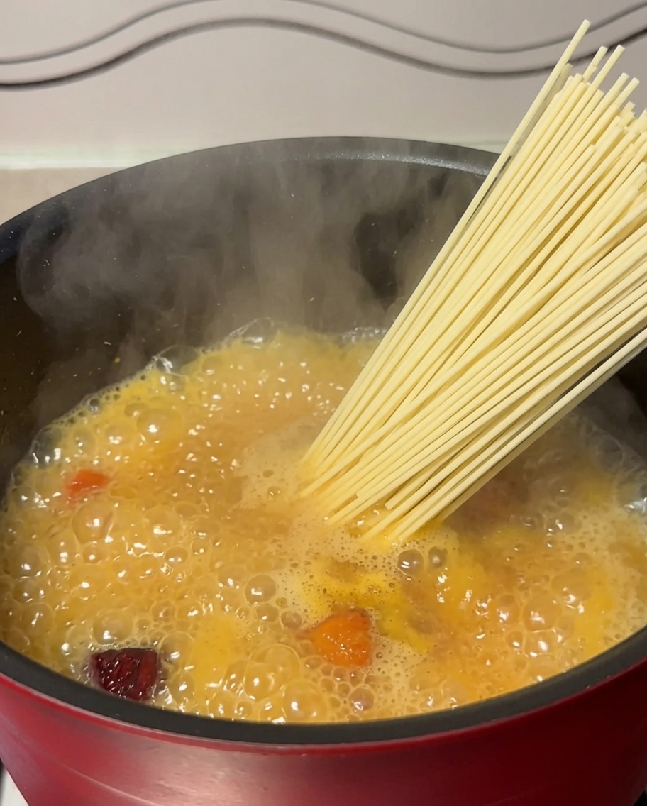 Nouilles séchées plongées dans une casserole de bouillon de poulet bouillant.