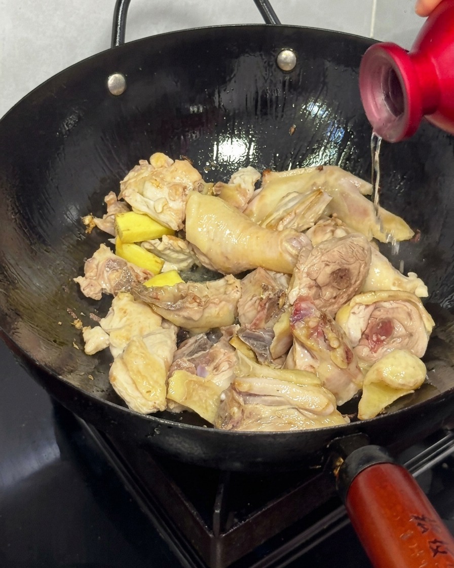 Verser du vin de riz dans un wok contenant le poulet doré et le gingembre.