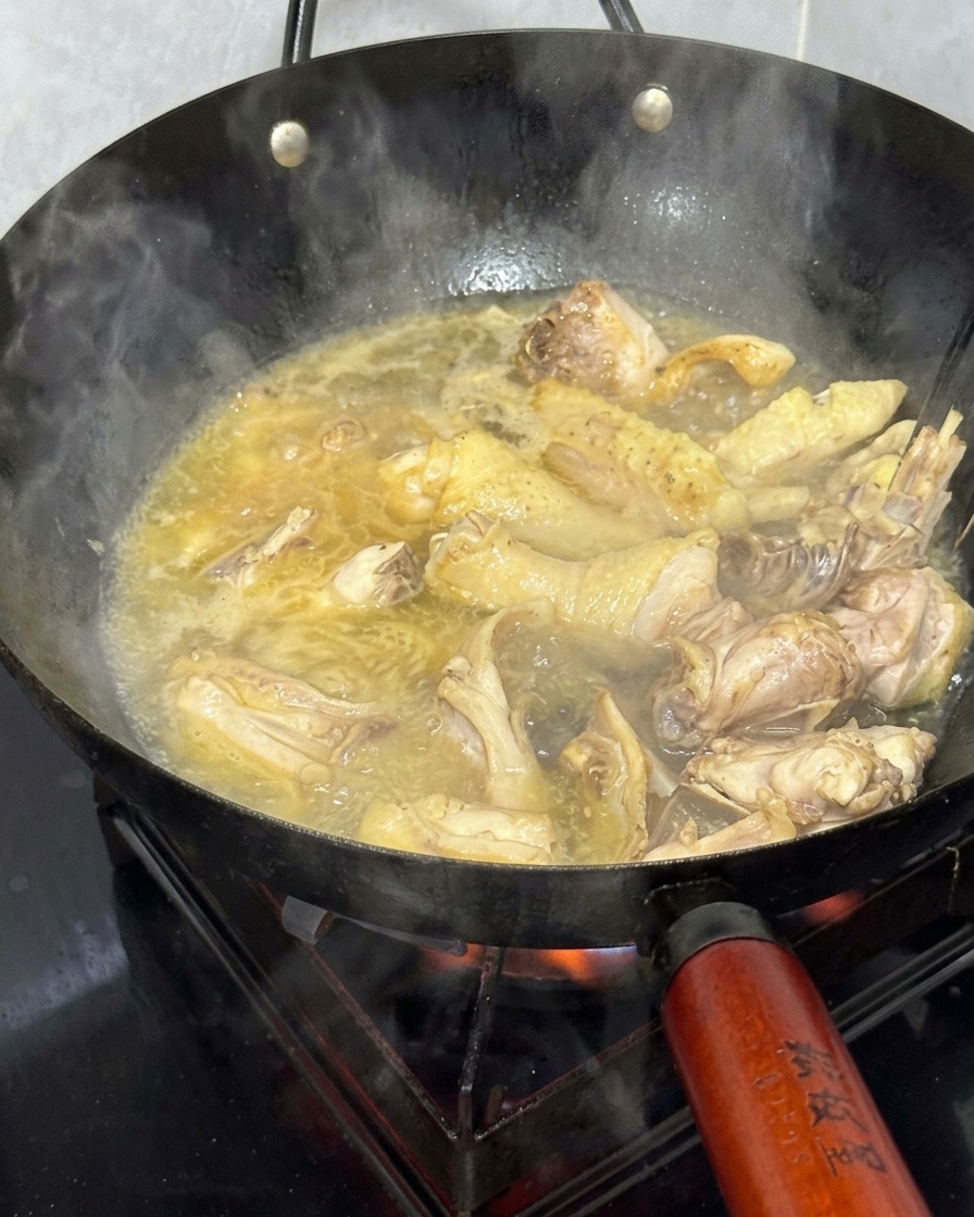 Morceaux de poulet mijotant dans un bouillon doré bouillonnant dans un wok.