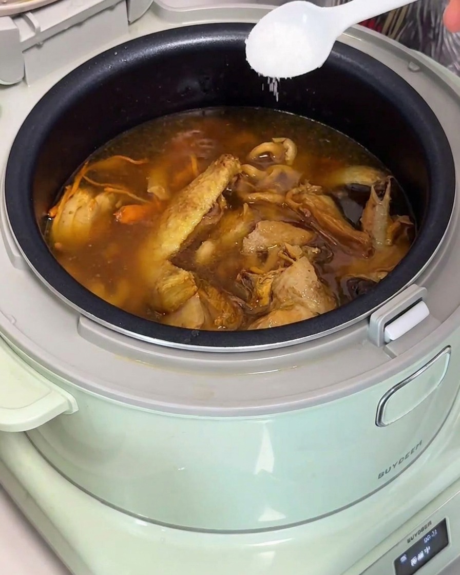 Ajout de sel dans une soupe de poulet aux champignons dans le cuiseur à riz.