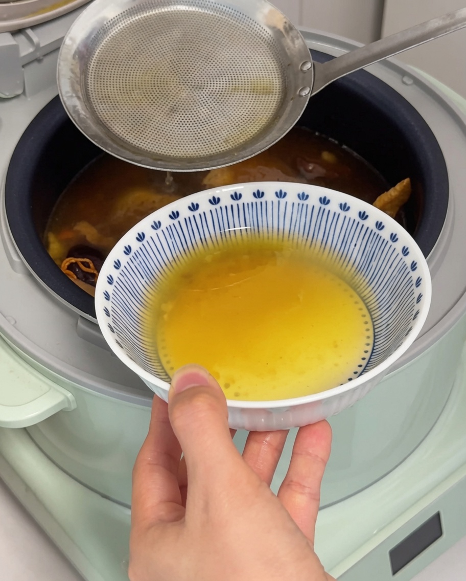 Une louche retirant une couche de gras doré à la surface du bouillon.