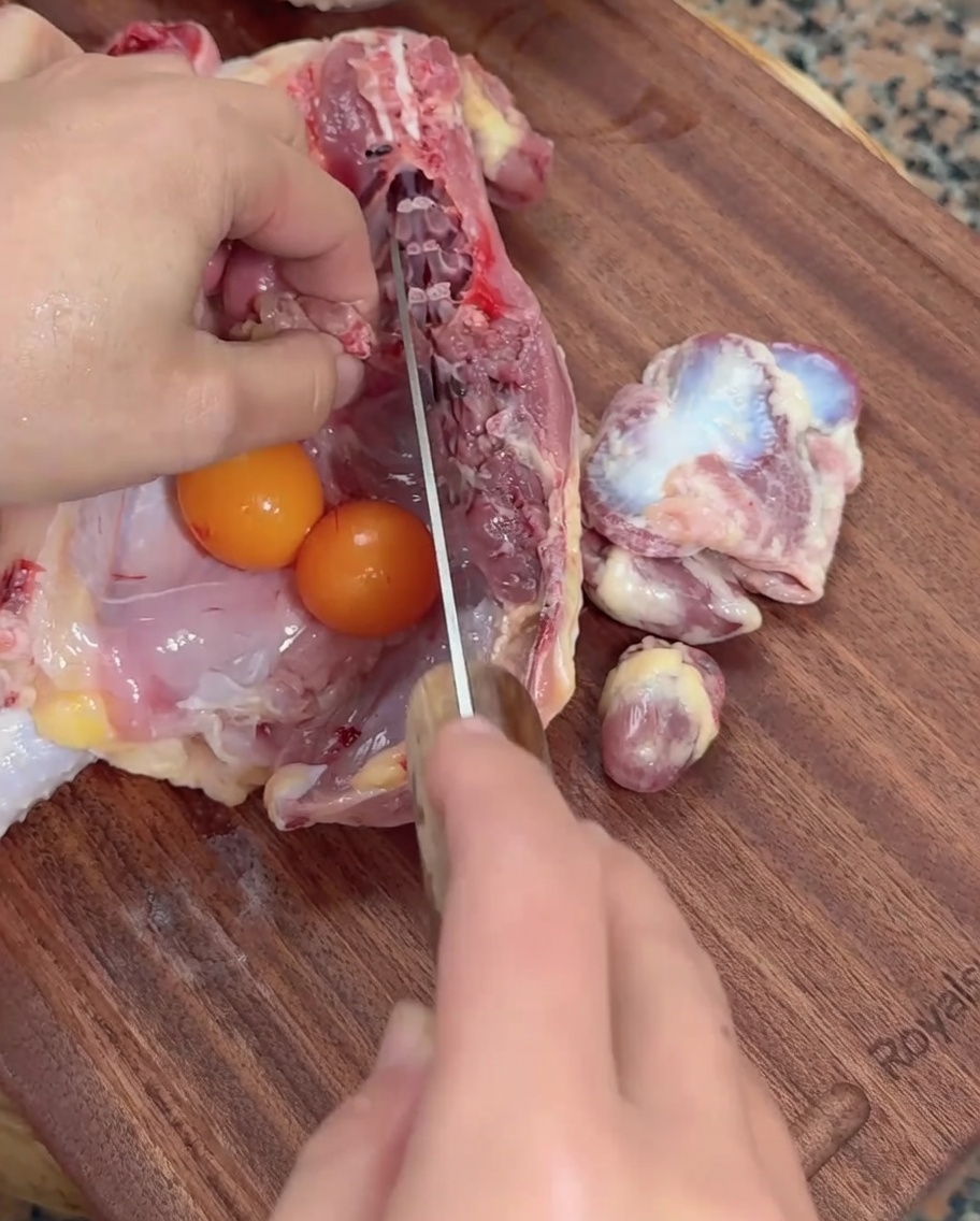 Mains utilisant un couperet pour inciser des abats de poulet crus à côté dœufs de poule non pondus sur une planche à découper en bois.