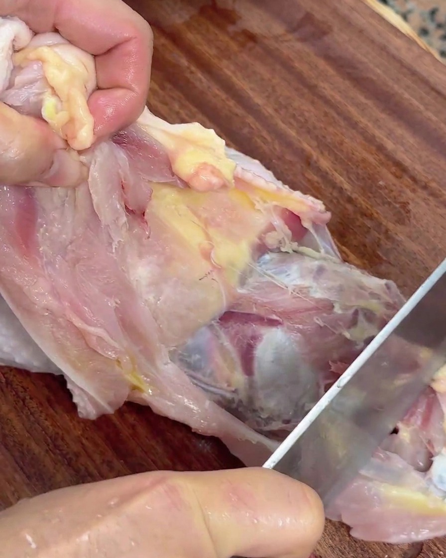 Mains tenant un poulet cru et utilisant un couteau pour séparer la viande de la carcasse.