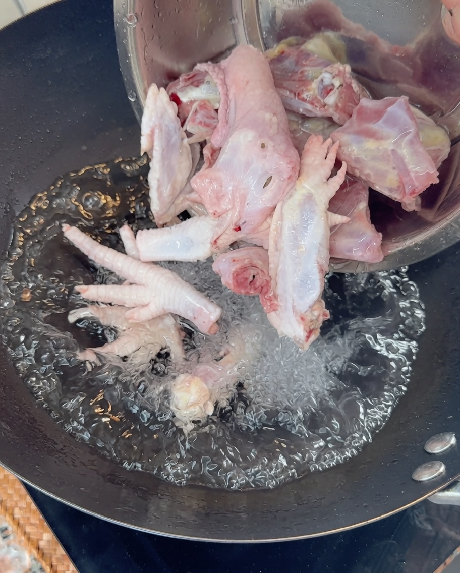 Verser des os et des pattes de poulet crus dans un wok deau bouillante.