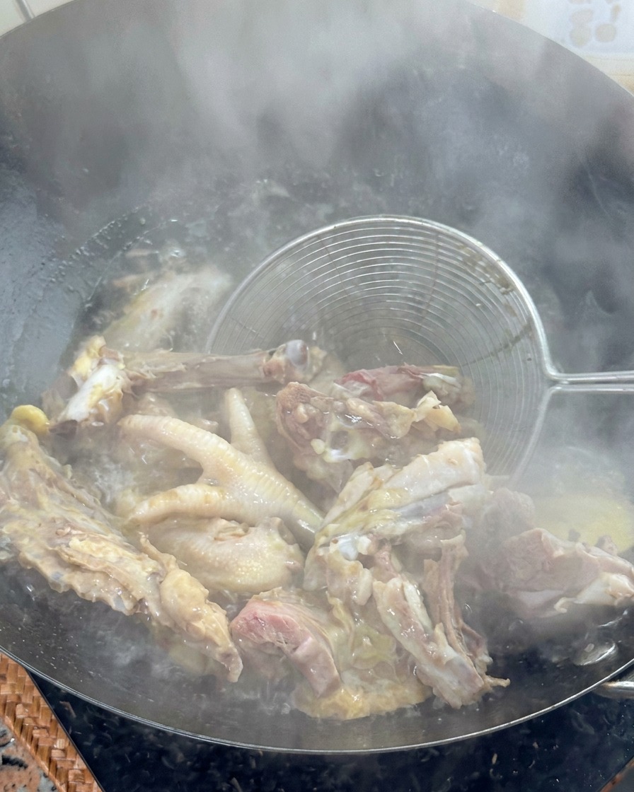 Une écumoire métallique soulevant des os de poulet blanchis dun wok deau bouillante.
