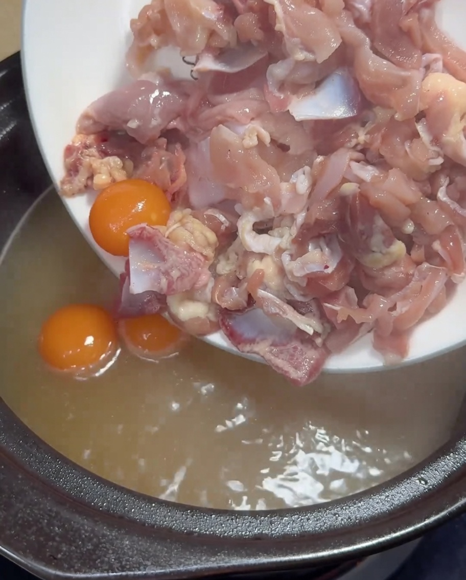 Fines tranches de poulet cru et jaunes dœufs frais ajoutés dans un pot de bouillon de poulet doré bouillant.