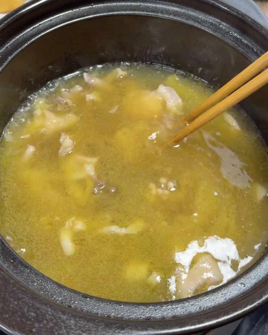 Des baguettes remuant délicatement les tranches de poulet et les jaunes dans la soupe frémissante.