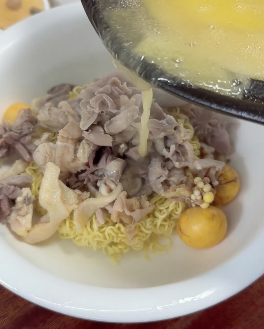Bouillon de poulet chaud et doré versé à la louche dans un bol de nouilles et de poulet.