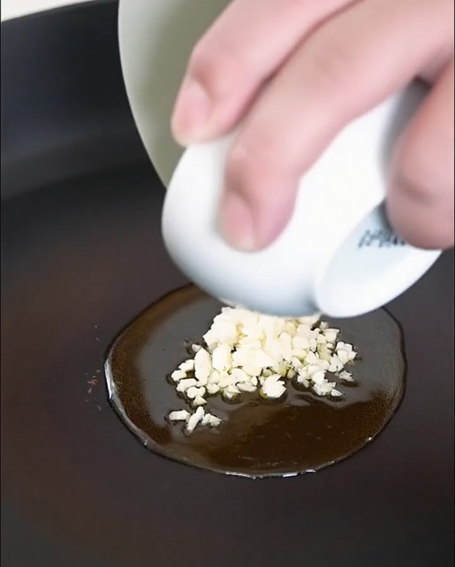 Ail et champignons émincés en train de dorer dans une poêle avec de lhuile dolive.