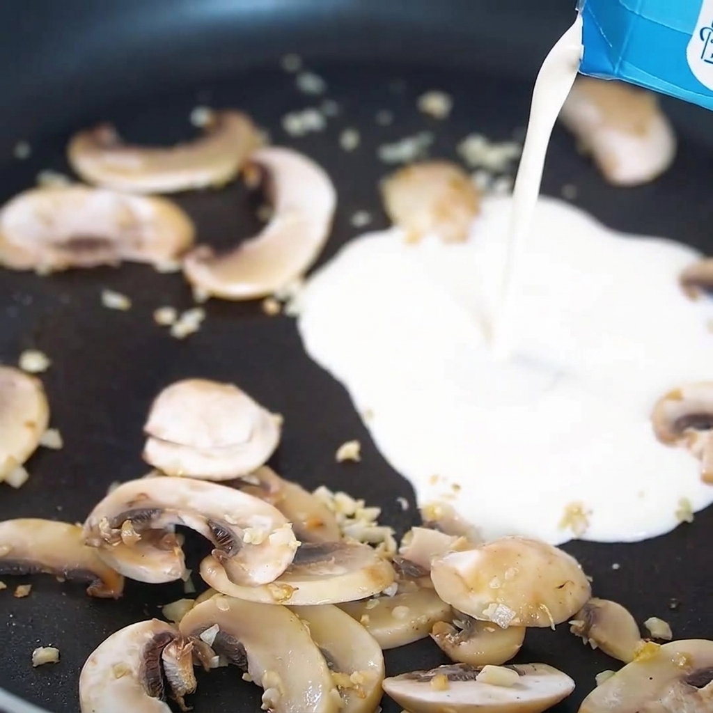 Crème versée dans une poêle contenant les champignons et lail cuits.