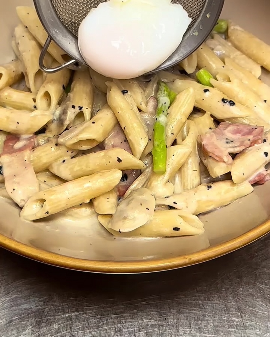 Pennes crémeuses déposées dans une assiette avec un œuf poché placé soigneusement au centre.