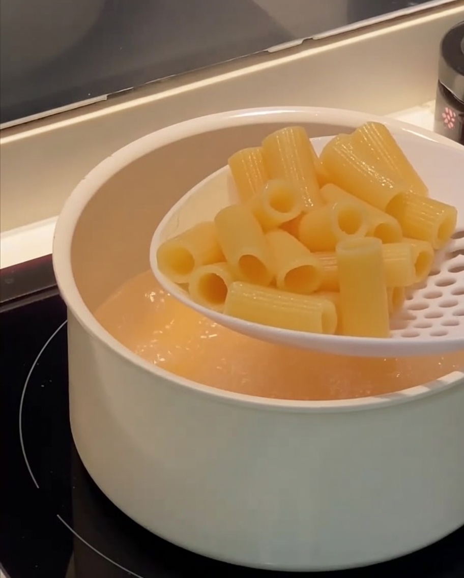 Une écumoire retirant les rigatoni cuits de leau bouillante.