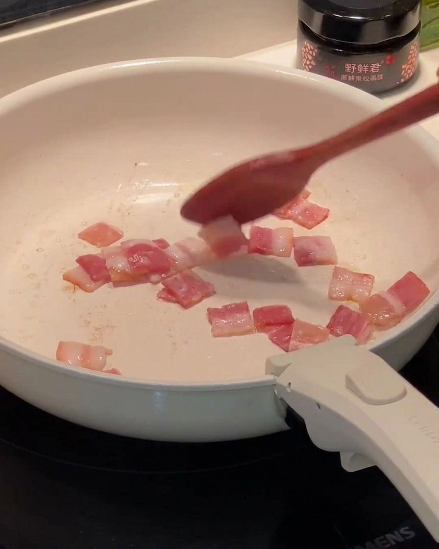 Bacon haché frit dans une poêle, avec le gras qui commence à se libérer.