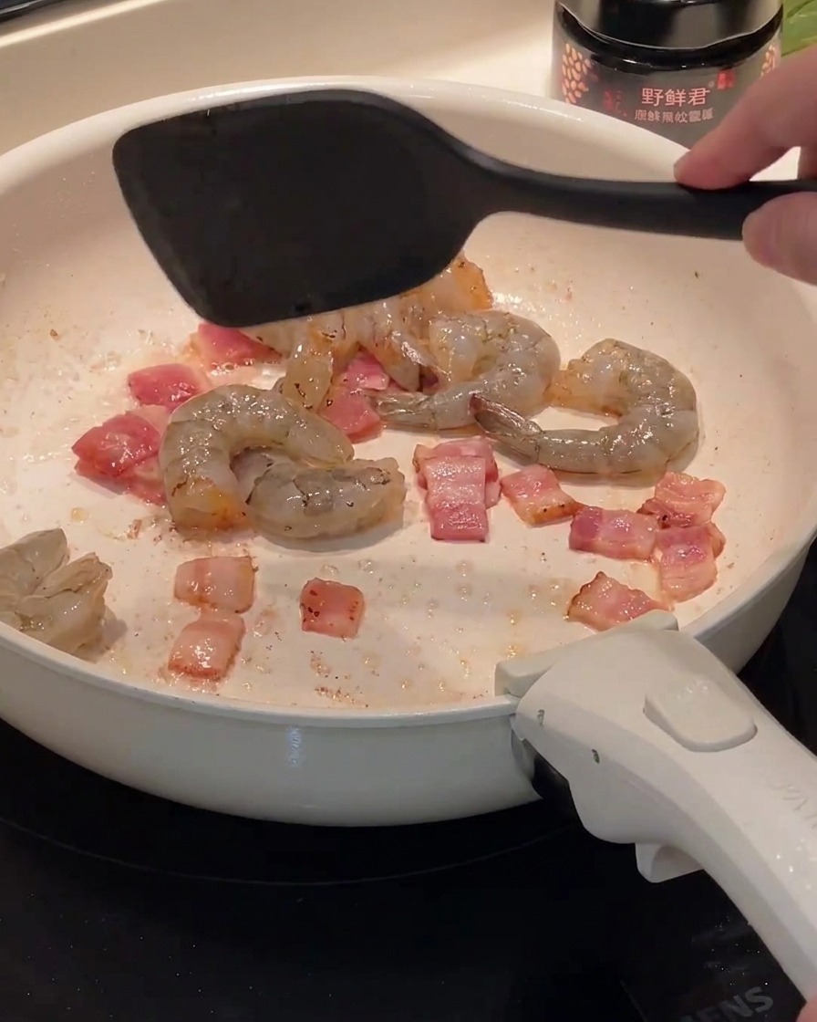 Crevettes crues ajoutées dans la poêle contenant les morceaux de bacon cuits.