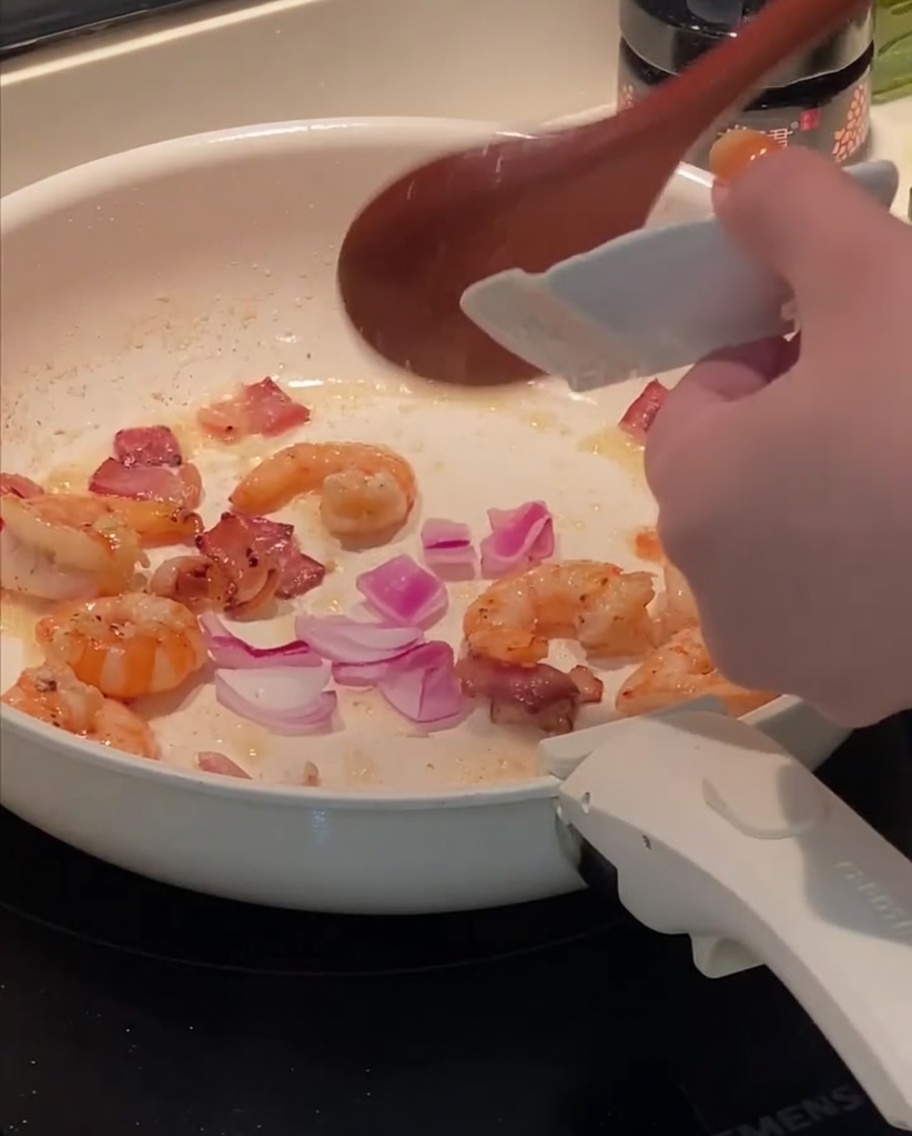 Oignon rouge haché ajouté à la poêle avec le bacon et les crevettes.