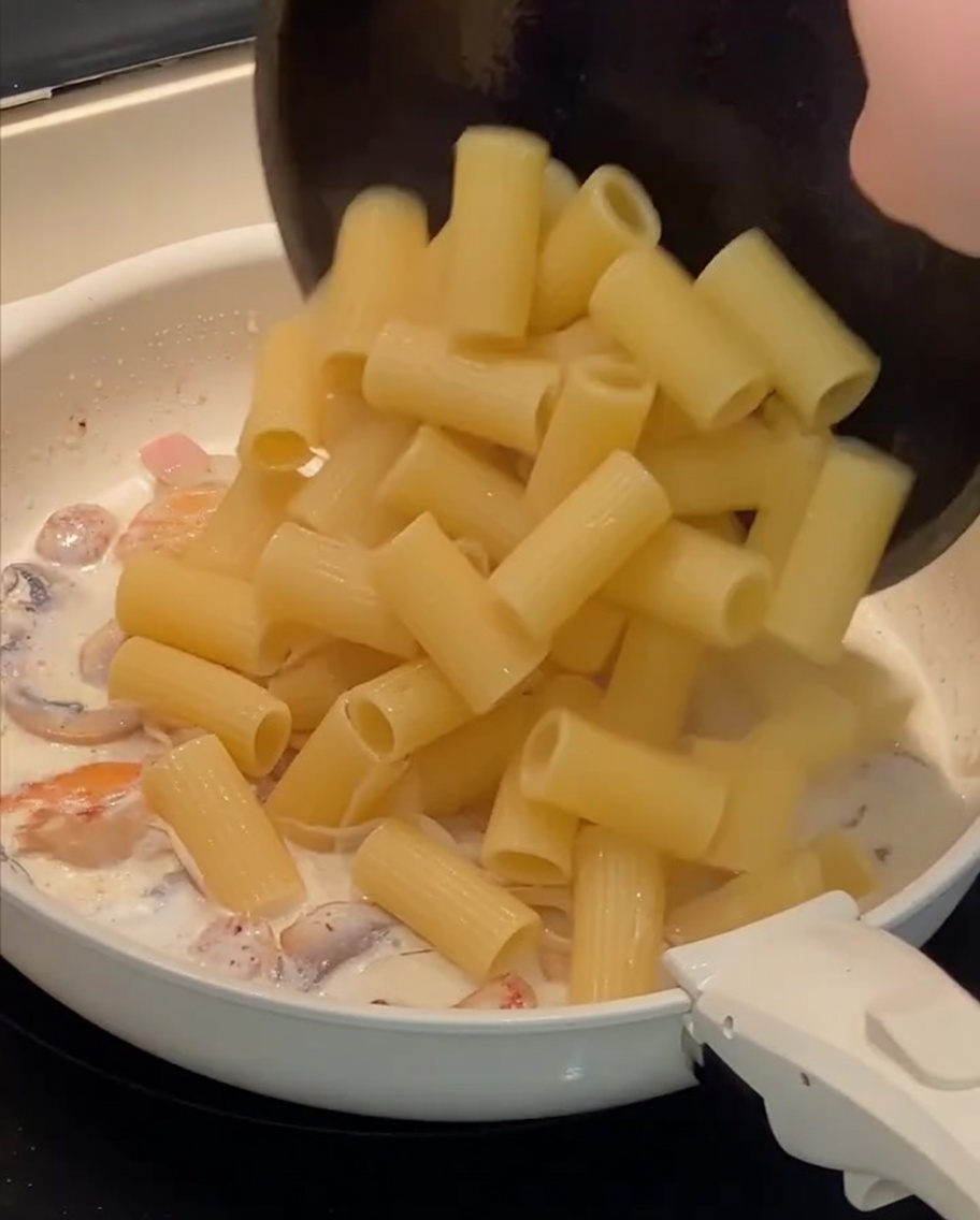 Rigatoni cuits ajoutés à la poêle avec la sauce crémeuse.