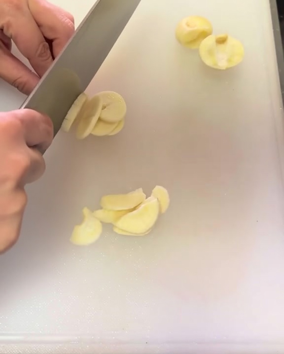 Gousses dail finement tranchées réparties sur une planche à découper blanche.