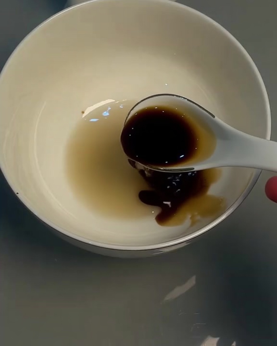 Sauce soja claire dans un bol blanc remuée avec une cuillère.