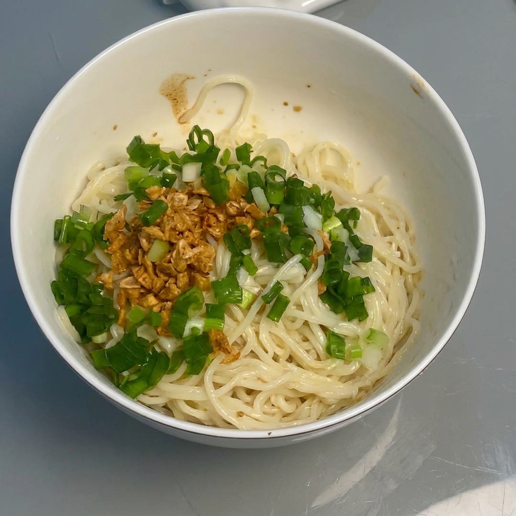Nouilles mélangées avec la sauce, lail et les oignons à laide de baguettes.