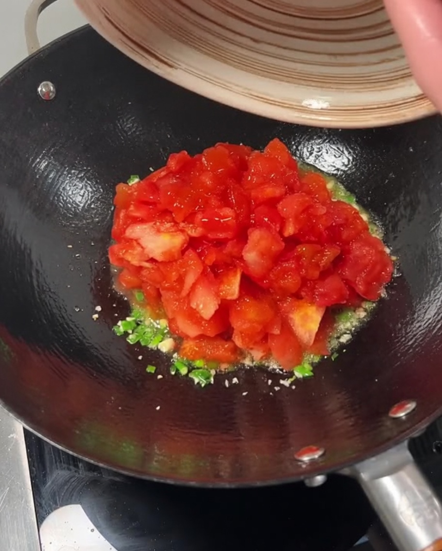 Tomates en dés versées dun bol dans un wok sur des oignons verts et de lail sautés.