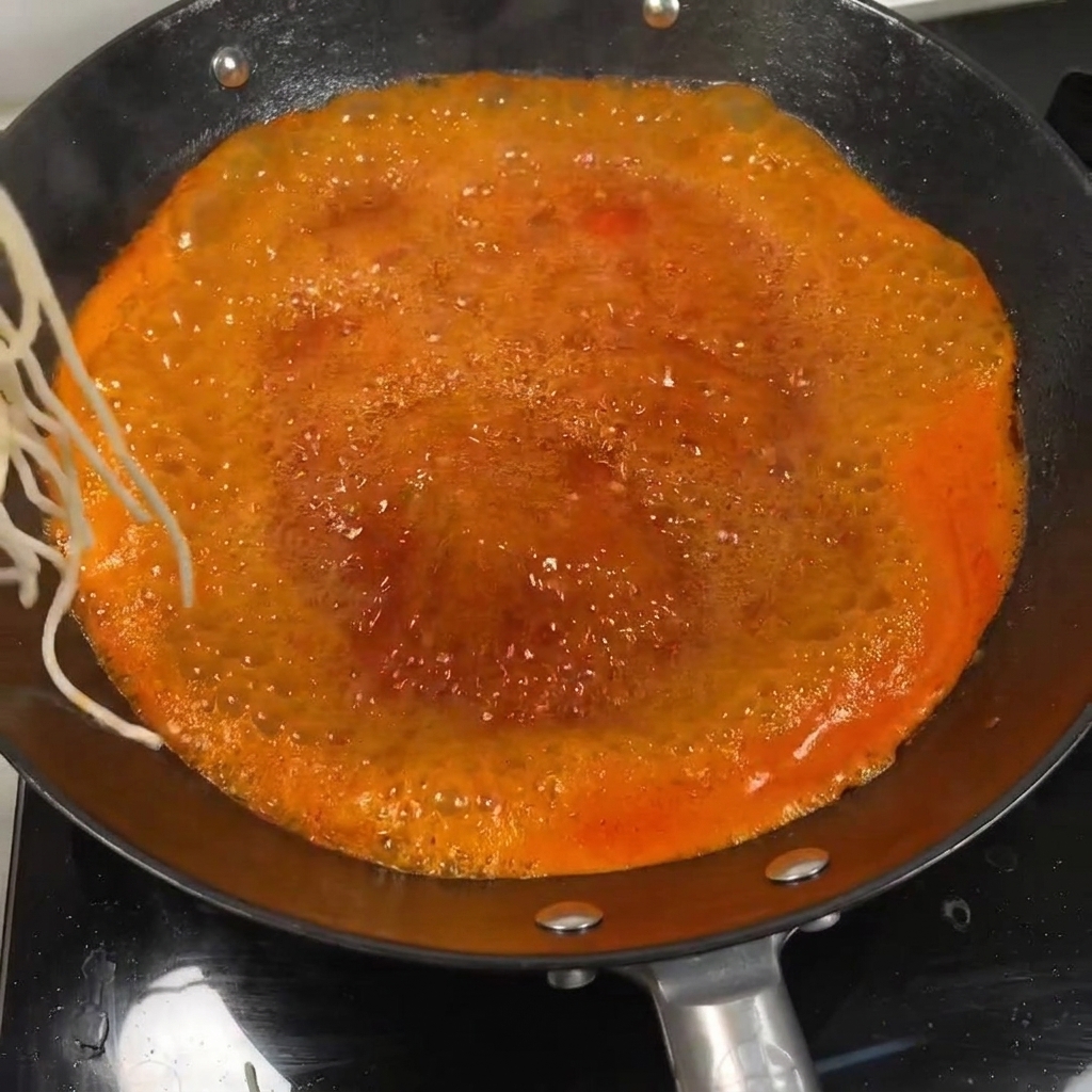 Nouilles plongées dans un bouillon de soupe à la tomate bouillonnant et coloré dans un wok.