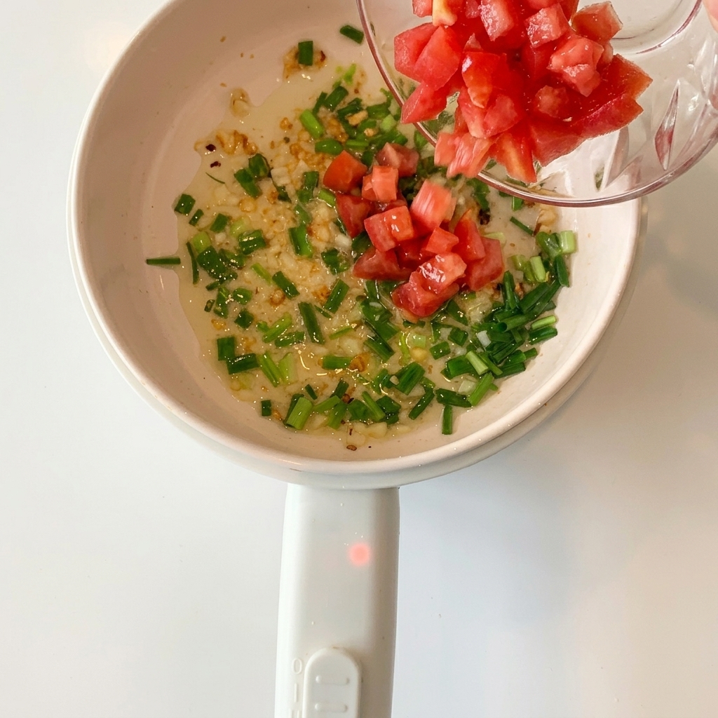 Tomates rouges en dés ajoutées dans la casserole contenant lail et les oignons verts sautés.