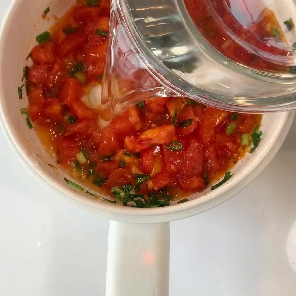 Eau claire versée dun bol en verre dans la casserole avec les tomates.