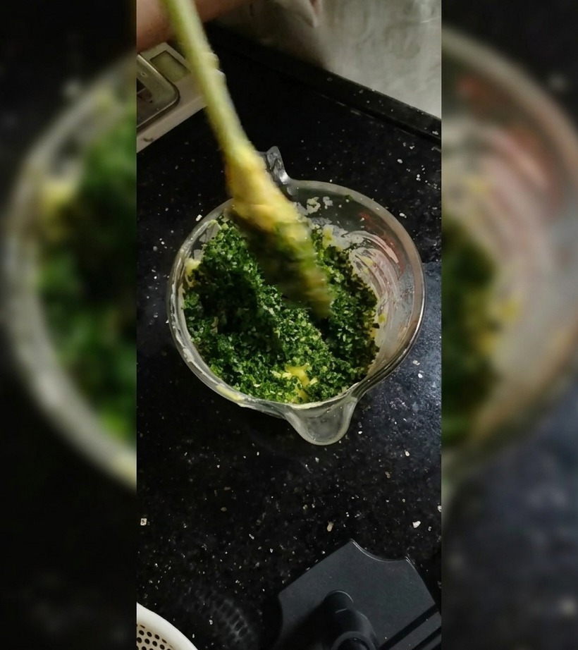 Une spatule en silicone mélange les herbes au beurre dans un bol en verre.