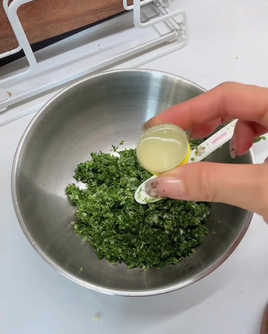 Jus de citron versé depuis une cuillère à mesurer dans un bol contenant le mélange aux herbes.