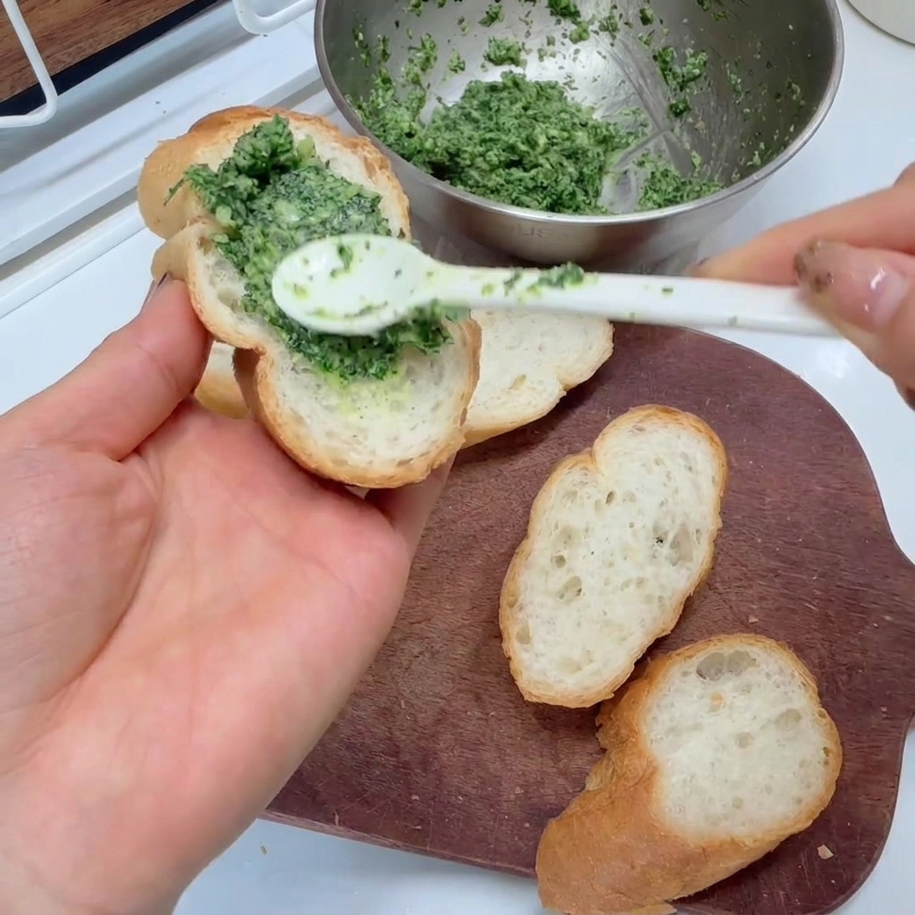 Tartinade verte aux herbes appliquée sur des tranches de baguette avec une cuillère.