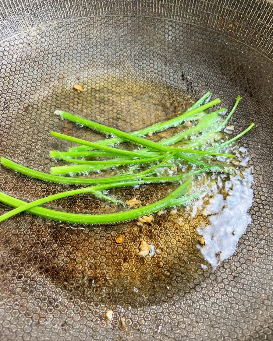 Tiges de persil frais ajoutées à lhuile infusée à lail dans le wok.