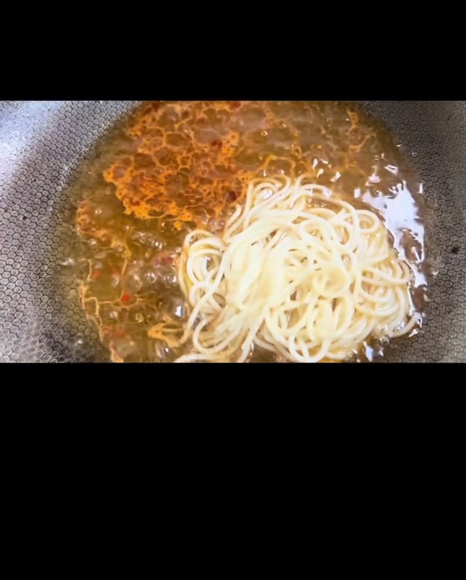 Spaghettis bouillis transférés dans le wok pour se mélanger à la sauce.