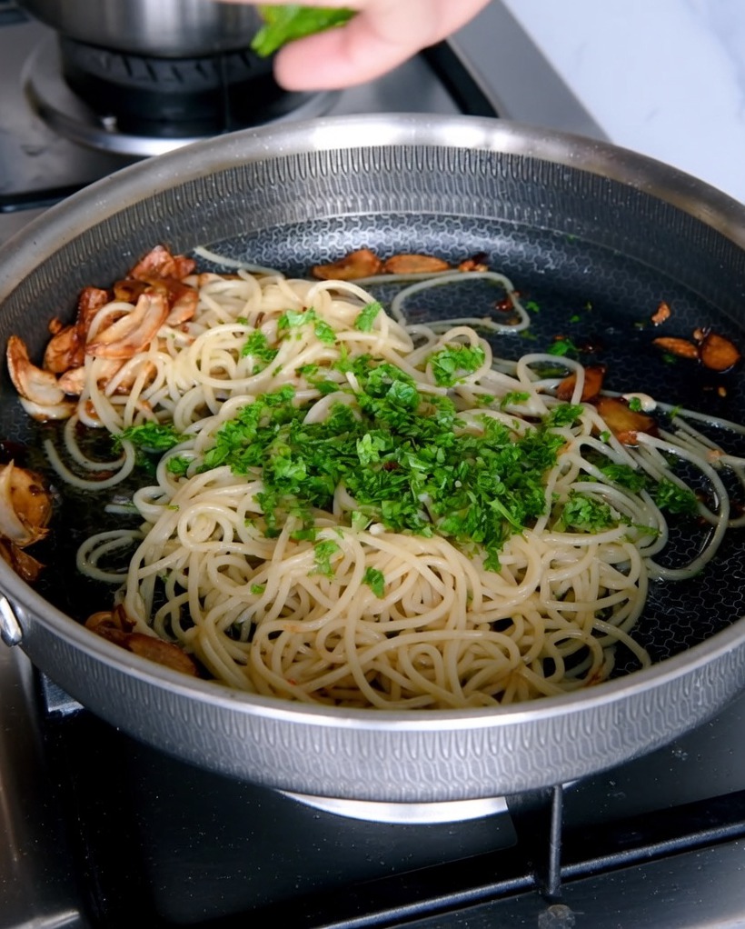 Persil frais haché ajouté à la poêle de spaghettis à lail.