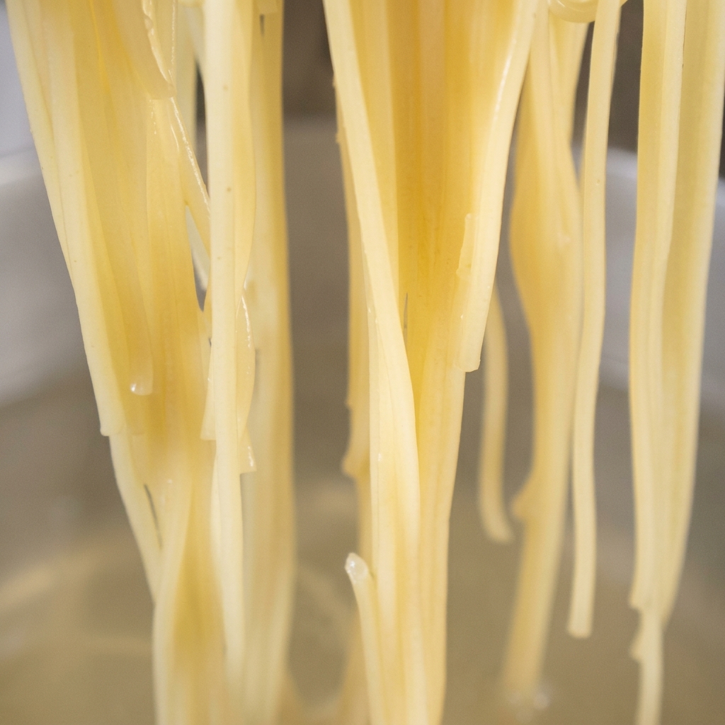 Nouilles spaghettis cuites ajoutées à une poêle avec de lail doré et de lhuile au piment rouge.