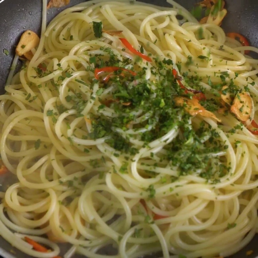 Persil frais haché parsemé sur le mélange de spaghettis, de piment et dail dans la poêle.