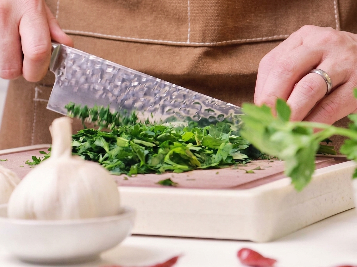 Persil frais vert finement haché sur une planche à découper en bois avec un grand couteau de chef.
