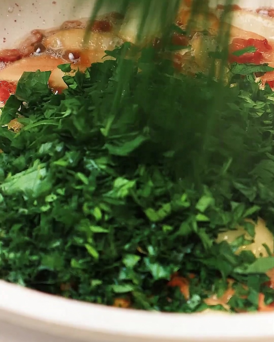 Persil haché ajouté à la poêle contenant lail et le bacon, remué légèrement pour combiner.