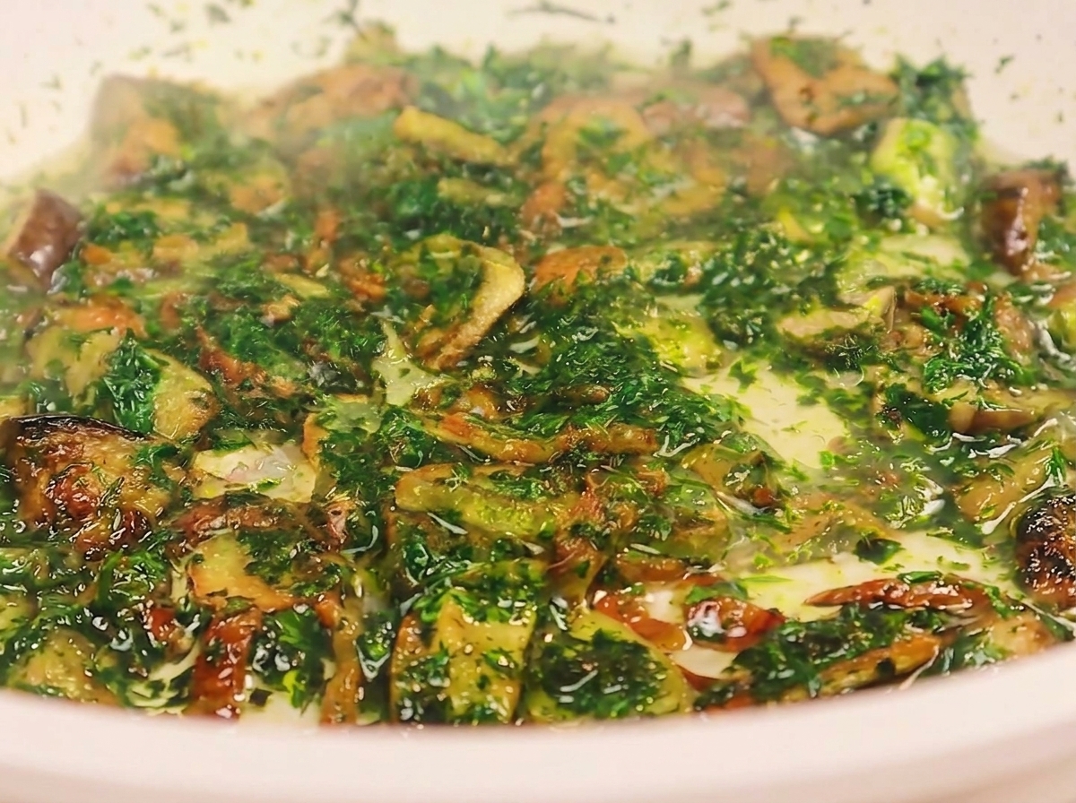 Une louche versant de leau de cuisson trouble dans une poêle contenant du bacon frit, de lail et du persil haché.